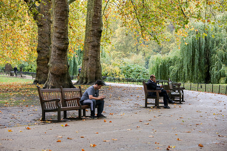 Two men sit on a bench at St James's Park in London, on a mild autumnal day.