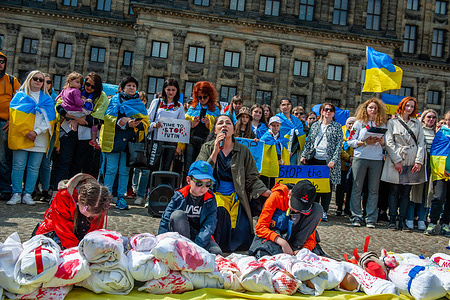 A group of children seen sitting in front of dolls covered in white blankets and fake bloodstains. The Ukrainian community in The Netherlands, mainly women and children gathered in the center of the city to draw the world's attention to the horrifying tragedies of children in Ukraine, caused by the Russian aggression. Within 21 days of war in Ukraine (as of March 16), at least 108 children were killed in shelling carried out by Russian Armed Forces, and more than 100 were wounded. During the protest, some of the women were holding dolls covered in a white blanket with fake bloodstains.