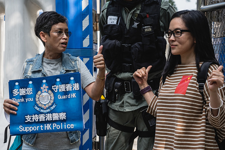 Pro-police supporters stand next to a policeman while making gestures outside a police station during the protest.
Over a hundred pro-police demonstrators gathered outside government offices in support of the Hong Kong Police Force. Supporters waves flags and placards while chanting various slogans in support of the police, who have come under intense scrutiny and criticism over their handling of the ongoing protests. While the police have been accused of misconduct multiple times over recent months, there still remains a strong contingent of police-supporters within the city.