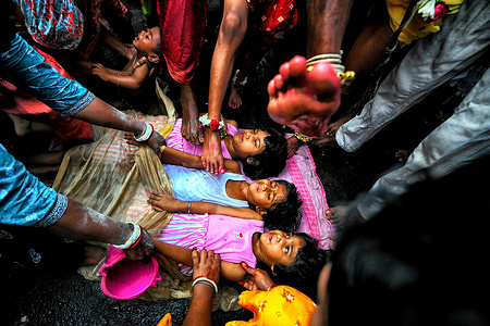 Kids seen lying on the street while the devotees step on them during the Gajan Festival. Gajan Festival is a Hindu Traditional Folk Festival celebrated mainly in the Eastern part of India at the end of Bengali year / Mid of April , where people dress up as different Hindu God & doing different ritual practices like Face painting , Piercing , Playing with fire to satisfy their belief / God for the wellness of the Family .