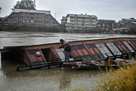 A Kashmiri man inspects a houseboat which capsized following heavy rains.
A flood alert has been sounded in Kashmir in the wake of continuous rains since Wednesday. The Irrigation and Flood Control Department of the state has issued the alert in several places after the water crossed the danger mark in different tributaries in Srinagar, Indian administered Kashmir.