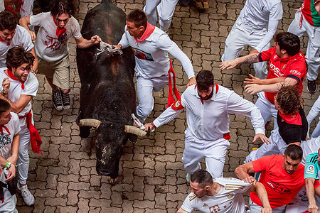 Several runners dressed in white and red run in front of the bull from the Fuente Ymbro ranch, along various sections of the route during the first running of the bulls of San Fermín 2025.
