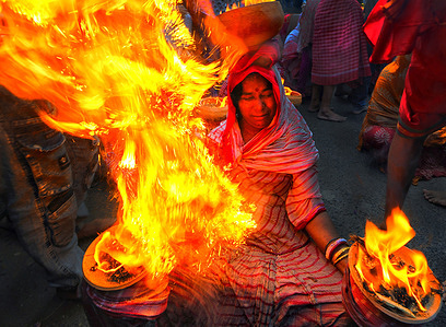 A hindu woman seen seated with a burning fire pot on her head and two burning fire plates in her hands as a Traditional ritual of worshipping Devi Sheetala. As per Hindu mythology Devi sheetala is being worshipped as she cures smallpox's, sores, ghouls, pustules and diseases. Hence Hindu people observe Fast for the whole day and doing different traditional practices like Dandi (Lying on Ground) and put burning Fire Pot on their heads while worshiping to Devi sheetala for betterment of their family members.
