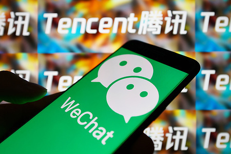 In this photo illustration the WeChat logo is seen displayed on a smartphone with a Tencent logo on the background.