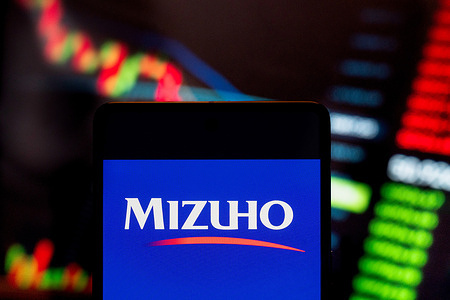 In this photo illustration, the Japanese multinational banking and financial services corporation Mizuho Bank logo seen displayed on a smartphone with an economic stock exchange index graph in the background.