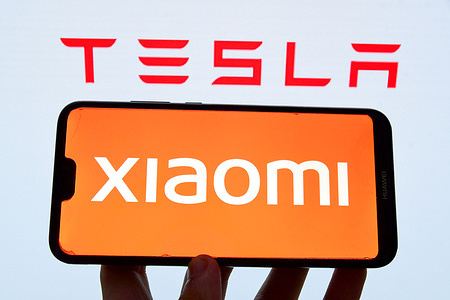 In this photo illustration, a Xiaomi logo is seen displayed on phone with Tesla logo in the background.