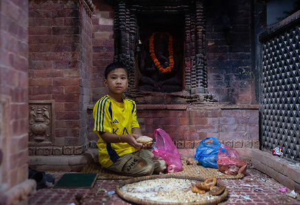 A child pays homage by making offerings at the chaitya (Buddhist shrine) and stupa during the festival. Devotees light butter lamps and offer prayers during a late-night procession around the historic town's sacred chaityas and shrines on the occasion of Gunhi Punhi (Janai Purnima). The traditional night walk sees local Newar families traversing ancient shrines past midnight to pay homage, offer incense, and make ritual offerings in memory of deceased family members.