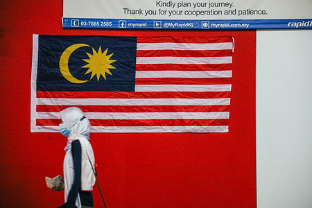 A Muslim woman wearing a protective face mask walks pass a Malaysian national flag at a transit train station. 
Malaysia reimposes CMCO "Conditional Movement Control Order" in Selangor state, Putrajaya and Kuala Lumpur for two weeks starting October 14, 2020 as cases spike amid third wave of Covid-19.