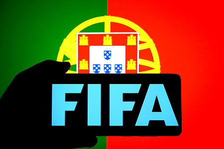 In this photo illustration, a FIFA logo is seen displayed on a smartphone with a Flag of Portugual in the background.