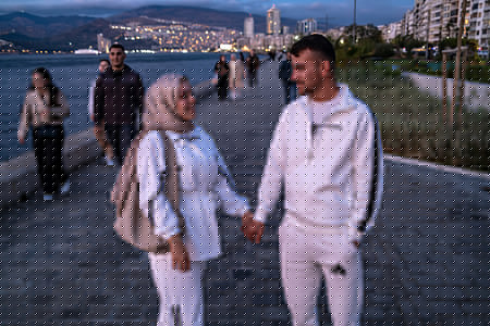 A couple hold hands while looking at each other at sunset. People watch the sun set over the Aegean Sea in Izmir, one of Turkey's three largest cities, as the evening sky glows with warm colours.
