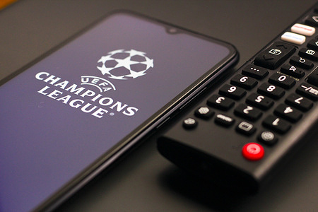 In this photo illustration, the UEFA Champions League (UCL) logo is seen displayed on a smartphone screen next to a TV remote control.