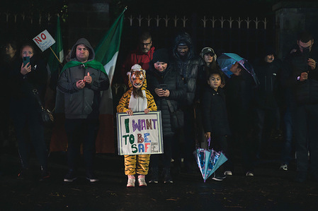 A young child wearing a tiger costume holds a sign reading "I want to be safe" in response to the sexual abuse of a ten-year-old girl in the arena, which sparked the outcry and subsequent nights of rioting. A peaceful vigil was held outside the fortified gates of the former Citywest Hotel, now serving as an IPAS centre for migrants, to honor a 10-year-old girl who was sexually assaulted in the area on October 20. The event stood in sharp contrast to the previous nights of rioting and violence at the same location, with attendees gathering quietly to pay their respects and call for justice.