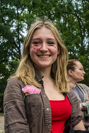 A young Guns N' Roses fan wears face paint under each eye, one depicting guns and the other, roses. The event, supported by Public Enemy and Guns N' Roses, brings their "Because What You Want & What You Get Are Two Completely Different Things" tour to PGE Narodowy in Warsaw, Poland, where they perform to a reportedly sold-out audience. Before the show, the bands' fans gather outside the stadium to buy merchandise, pose for photographs, and soak in the atmosphere.
