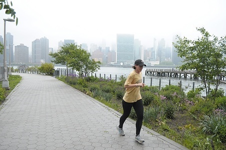 A person jogs in a park by the East River in Long Island City, Queens, New York City as a view of Manhattan is seen in the background.