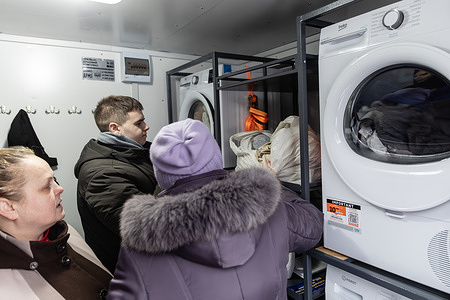 Residents seen using washing machines inside a mobile Solidarity Point to clean clothes during power outages caused by infrastructure strikes. A specialized mobile assistance point, the "Solidarity Point" has begun operating to support residents who have been without electricity, heating, and water for weeks following massive strikes on infrastructure. The mobile complex consists of several units one where citizens can warm up, obtain hot water, charge their devices, and another equipped with washing machines and dryers to address basic hygiene needs. This initiative aims to restore essential living conditions during the severe energy crisis by adapting technical solutions previously developed for frontline support to meet civilian needs. Given the high demand for these services, the project is set to scale up and deploy mobile stations to other districts of the capital where the utility situation remains most critical.