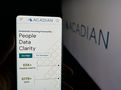 In this photo illustration, a person is holding a smartphone with the webpage of US company Acadian Asset Management Inc. on screen in front of logo.