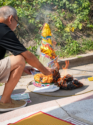 A man is seen burning Chinese spirit paper offerings, sending symbolic goods to his ancestors during the Qingming Festival at Jing Gong Cemetery. Qingming Festival, also called Tomb-Sweeping Day, is a traditional Chinese festival to honor ancestors. In Thailand, it is observed by the Thai-Chinese community. Families visit graves, clean tombs, and make offerings such as food, tea, incense, and paper items, focusing on respect, remembrance, and family ties across generations.