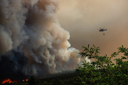 A helicopter carrying a Bambi bucket flies over a large wildfire to extinguish the fire near Miren. Over a thousand firefighters with air support from a Croatian Canadair firefighting airplane, three Slovenian helicopters, one Austrian helicopter, and a Slovenian army Pilatus PC-9 airplane battled a large wildfire that broke out four days ago and has intensified in the Karst region of Slovenia. Residents in five villages in the area were already evacuated.