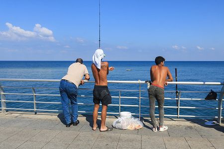 A fisherman casts a fishing rod into the sea on a hot sunny day in Beirut.