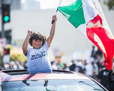 A young boy cheers from the sunroof of a car while waving a Mexican flag during an anti-ICE demonstration in downtown Los Angeles. Demonstrators temporarily blocked traffic demanding for the abolition of ICE and broader immigrant rights protections prompting a heavy police response.