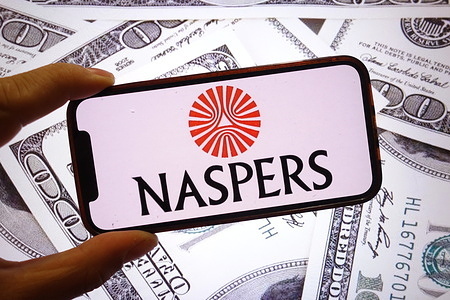 In this photo illustration, the Naspers company logo is seen displayed on a smartphone screen with United States dollar banknotes in the background.