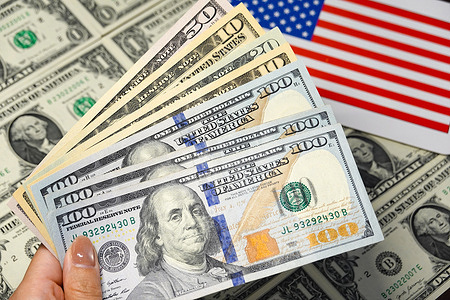 In this photo illustration, a hand holds several U.S. dollar bills with the American flag in the background.
