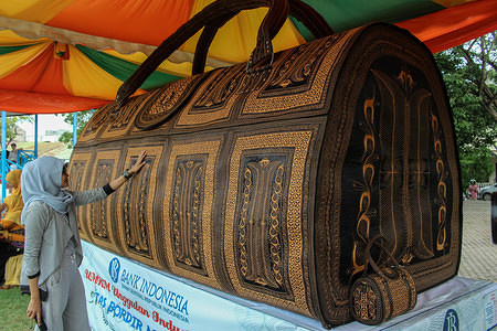 A woman seen touching the world largest handbag.
This large handbag is the work of the Acehnese scouted by the Bank of Indonesia has been registered as the World Record Museum (MURI) on November 12, 2017, because its unique value is united with Aceh's door motif which is characteristic of Acehnese society culture. The goal is to reduce the unemployment rate and accelerate the economic growth of the wider community.