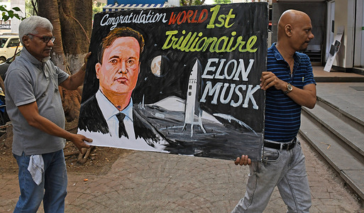 Teachers from Gurukul school of art carry back a painted poster congratulating businessman Elon Musk on becoming world's first trillionaire, outside their art school in Mumbai. Businessman Elon Musk became world's first trillionaire after the stock of SpaceX, his aerospace and AI company made a record breaking public debut on the Nasdaq stock exchange.