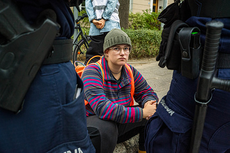 A climate activist wearing an orange vest sits on the side of the road surrounded by the police, after having been removed from the place of demonstration. Activists from the environmental action group Last Generation (Ostatnie Pokolenie) blocked vehicle access to the Polish parliament in Warsaw. Wearing orange vests, the activists glued their hands on the road, and others carried banners proclaiming the government is stealing their future. The action is designed to raise awareness of the climate crisis through disruption and is one of many designed to advocate for cheaper and wider public transport options. The group are demanding that the government shifts 100% of the money allocated for new expressways to regional public transport, and introduces a low-cost, 12.94 United States Dollar ticket for public transport throughout Poland. The series of road blocks take place on the week that Polish students return to school. "People must demand change" they state, "otherwise the government will continue to disregard our basic safety."