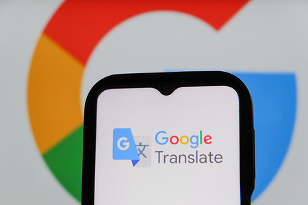 In this photo illustration, the Google Translate logo is seen displayed on a smartphone screen with a Google Logo in the background.