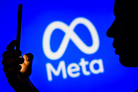 In this photo illustration, a woman's silhouette holds a smartphone with the Meta Platforms, Inc. logo in the background.
