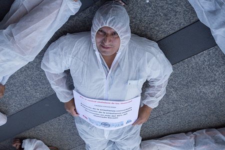 An activist seen laying on the ground dressed in a white overall holding a posters during a protest at the Bank of Spain demanding greater citizen control over the financial system and denouncing the suicides caused by 10 years of economic crisis.