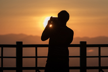 A tourist takes a photo of the sunrise during winter as fog covers the city.