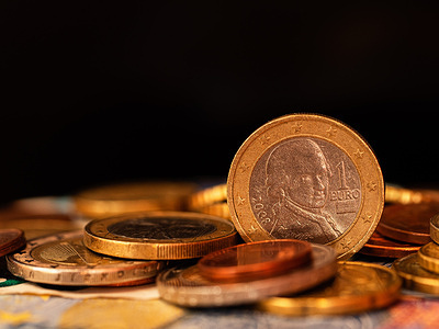 In this photo illustration, the reverse side of the 1 Euro 2008 coin from Austria depicting a portrait of Mozart seen among various coins with a black background.