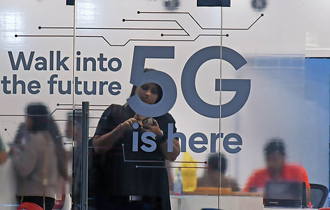 A woman checks her mobile phone inside a mobile service provider store advertising 5G service in Mumbai. 5G is fifth generation of cellular technology, a hundred times faster than 4G which will help in creating opportunities for people and businesses.