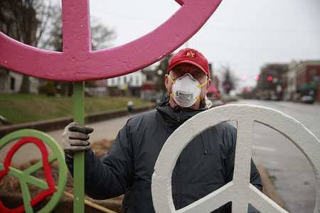 BLOOMINGTON, UNITED STATES - MARCH 18, 2020: A group of anti-war protesters gather for their weekly protest, with one wearing a mask, during the Covid-19/Coronavirus emergency in Bloomington. The Bloomington Peace Action Coalition has been protesting every Wednesday for an hour on Wednesday afternoons since the United States invaded Afghanistan in 2001 to begin the War on Terrorism.