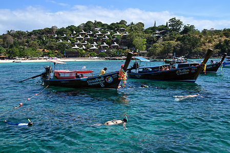 Foreign tourists snorkel in the clear waters of Ton Sai Bay beside a traditional long-tail boat, a popular mode of transport around Koh Phi Phi Don.