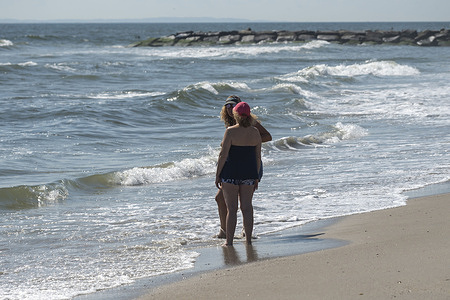 Beachgoers stand with their feet in the water and talk on a warm autumn day at Rockaway Beach on September 26, 2025 in the Queens borough of New York City.