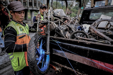 Sanitation workers lift the charred remains of a motorcycle onto a pickup truck outside the parliament and police headquarters after overnight protests turned violent. Overnight demonstrations turned violent after a motorcycle taxi driver was run over by a police armored vehicle, fueling wider anger over parliamentary salaries, state spending priorities, unqualified officials, inflammatory remarks, and the government’s free meal policy.