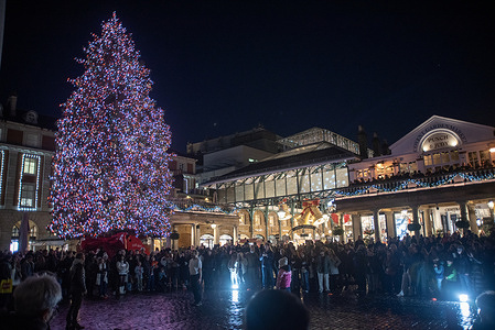 Crowds enjoy the show of the street acrobats outside the Covent Garden in London. Thousands of tourists and locals enjoys one of the most iconic London Christmas decorations at the Covent Garden. It is world-famous festive installation with 40 gigantic bells with bows, 12 very large baubles and 8 disco balls inside the Market building and the 16.7 meters tall (55 feet) Christmas tree outside.