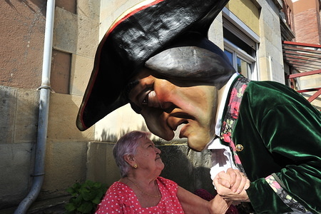 The kiliki named Caravinagre greets a resident of Casa Misericordia during the festivities.
San Fermín festivities celebrate the confinement of the bulls of the cattle ranch. The Palmosilla (run of the bulls), was settled with no one injured by a bull horn and the morning hours passed with the visit of the big heads to the house of Misericordia making a fun morning among the elderly.