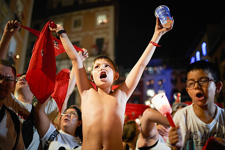 A child raised his arms while the other holds a candle, sing "Pobre de Mí," marking the end of the San Fermin 2026 festivities. As the clock strikes midnight on July 14, the San Fermín festival in Pamplona, Spain, concludes with the moving Pobre de Mí closing ceremony, where thousands of emotional festival-goers gather in the dark holding lit candles to softly sing a lament for the end of the festivities. Amidst the late-night goodbyes, the streets light up with the Toro de Fuego (fire bull), a mechanical or wooden bull frame carried by a runner that shoots off a spectacular array of harmless sparks and fireworks into the crowded town square.