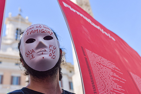 A protester wears a mask with inscriptions and carries a placard during the protest against precarious working conditions in Italy. The protest was led by insecurely employed university workers, mainly researchers, opposing a proposed law that would worsen job insecurity.