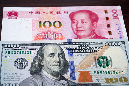 A red-and-gold Chinese ¥100 banknote with Mao Zedong’s portrait overlaps a US $100 bill featuring Benjamin Franklin.