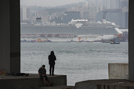 HONG KONG, CHINA, FEBRUARY 8, 2020:
Men fish while behind stands at large the Dream World cruiser docking at Kai Tak Cruise Terminal in Kowloon Bay, Hong Kong. Authorities are keeping 3,600 passengers and crew members under quarantine