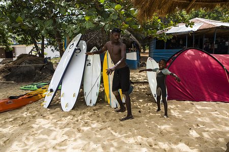 A man and a kid exercising next to surf boards. 
In Bureh Beach, 70 kilometers from Freetown, there is a surfing camp, where the kids forget the daily miseries while riding the waves.