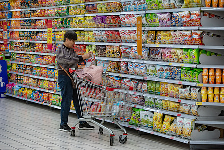 A woman stands by a snack shelf in a supermarket, picking items with a shopping cart full of goods beside her. China's consumer price index (CPI), a main gauge of inflation, was down 0.3 percent year-on-year in September 2025, data from the National Bureau of Statistics showed on Wednesday, October 15, 2025.