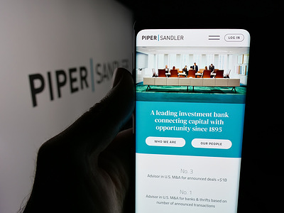 In this photo illustration, a person is holding a smartphone with the web page of US investment bank Piper Sandler Companies on screen in front of logo.
