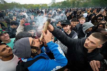 A man seen smoking an oversized cannabis cigarette while surrounded by onlookers. Thousands gathered at Speakers’ Corner in Hyde Park for the annual “420” rally, a major event advocating cannabis culture and drug policy reform in the UK. Participants arrived from midday and marked 4:20 p.m. with a collective “light-up,” filling the park with smoke. Police maintained a strong presence, making several arrests while enforcing regulations during the unauthorized gathering.