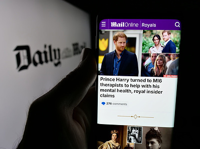 In this photo illustration, a person is holding a smartphone with the web page of British tabloid newspaper company Daily Mail on screen in front of logo.
